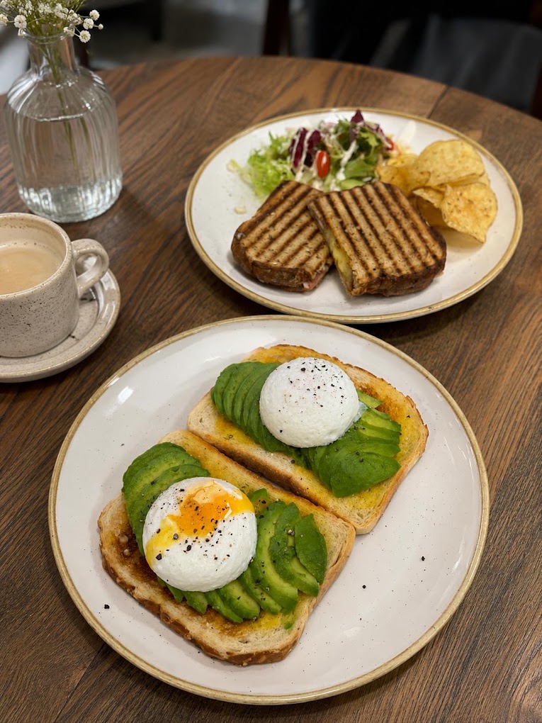 Avocado and poached egg on toast, with a grilled panini and a flat white