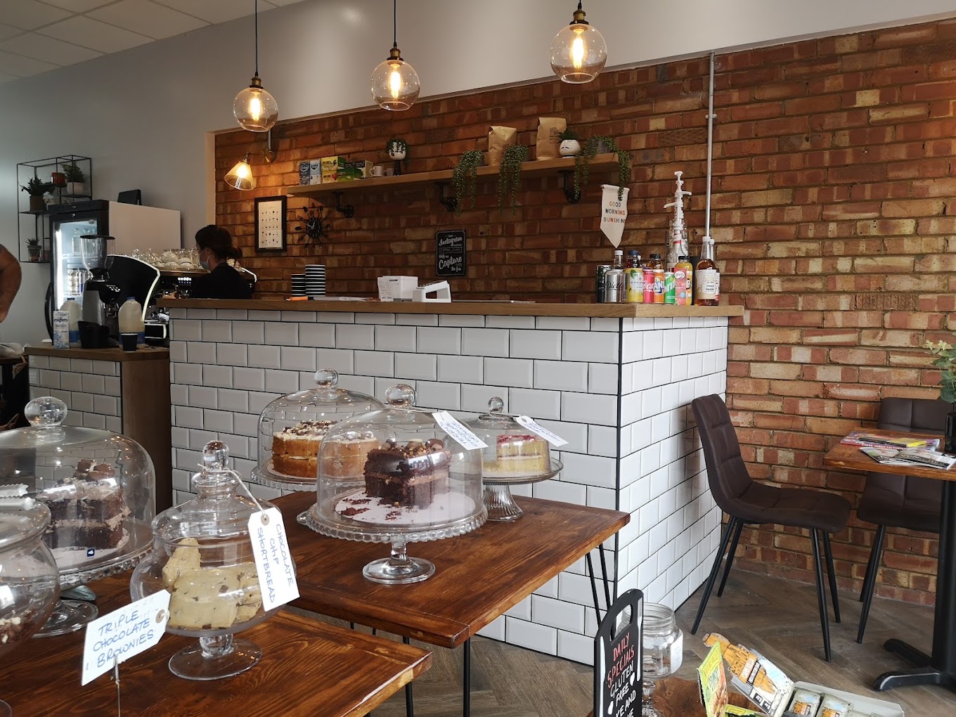 Cake stands under glass domes on the counter, labelled triple chocolate brownies and chocolate chip shortbread