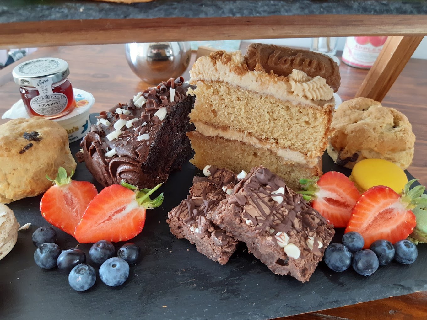 A tiered afternoon tea stand with cake, brownies, macarons, scones and fresh fruit