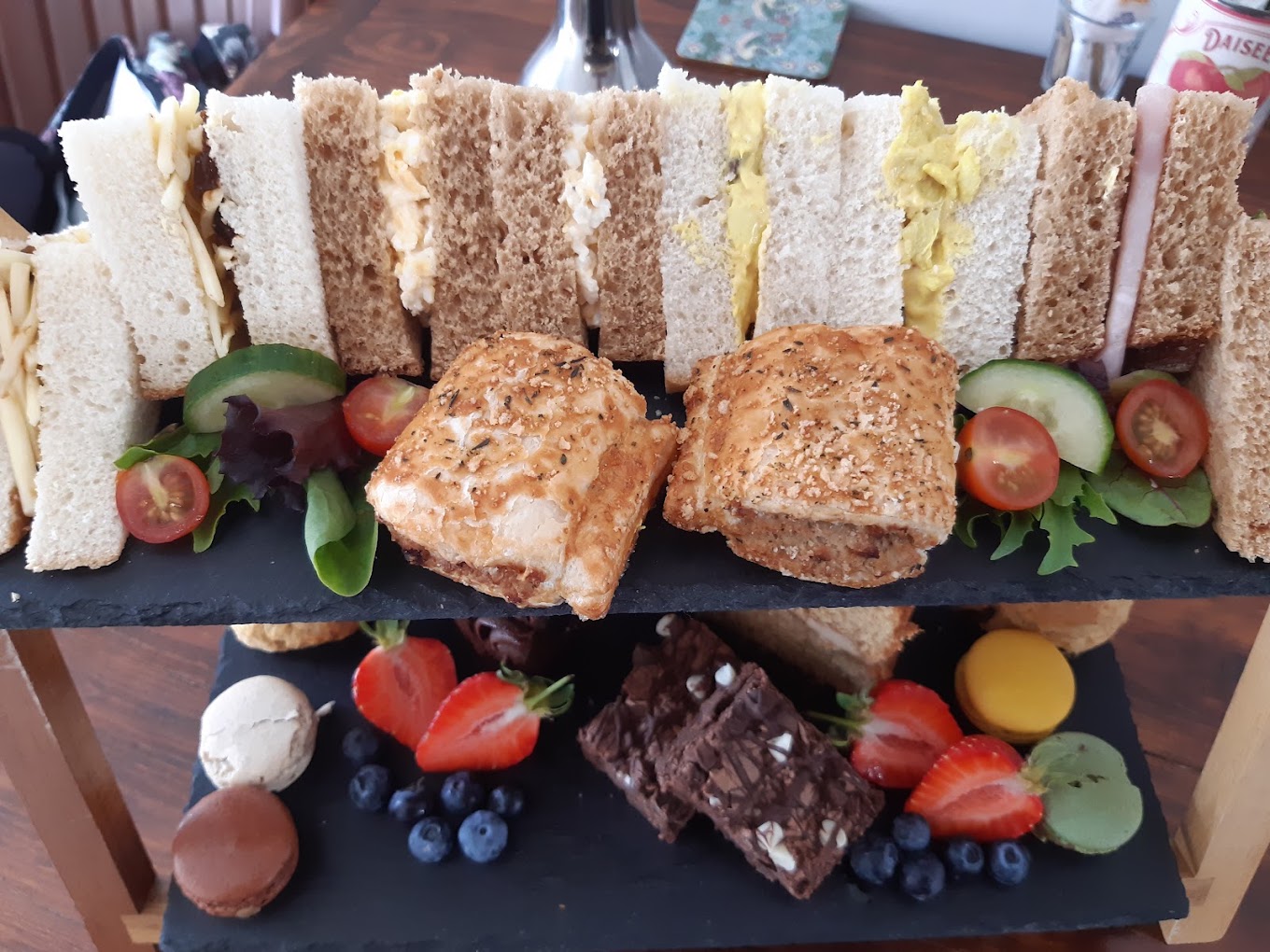 A second afternoon tea stand with finger sandwiches, sausage rolls and macarons